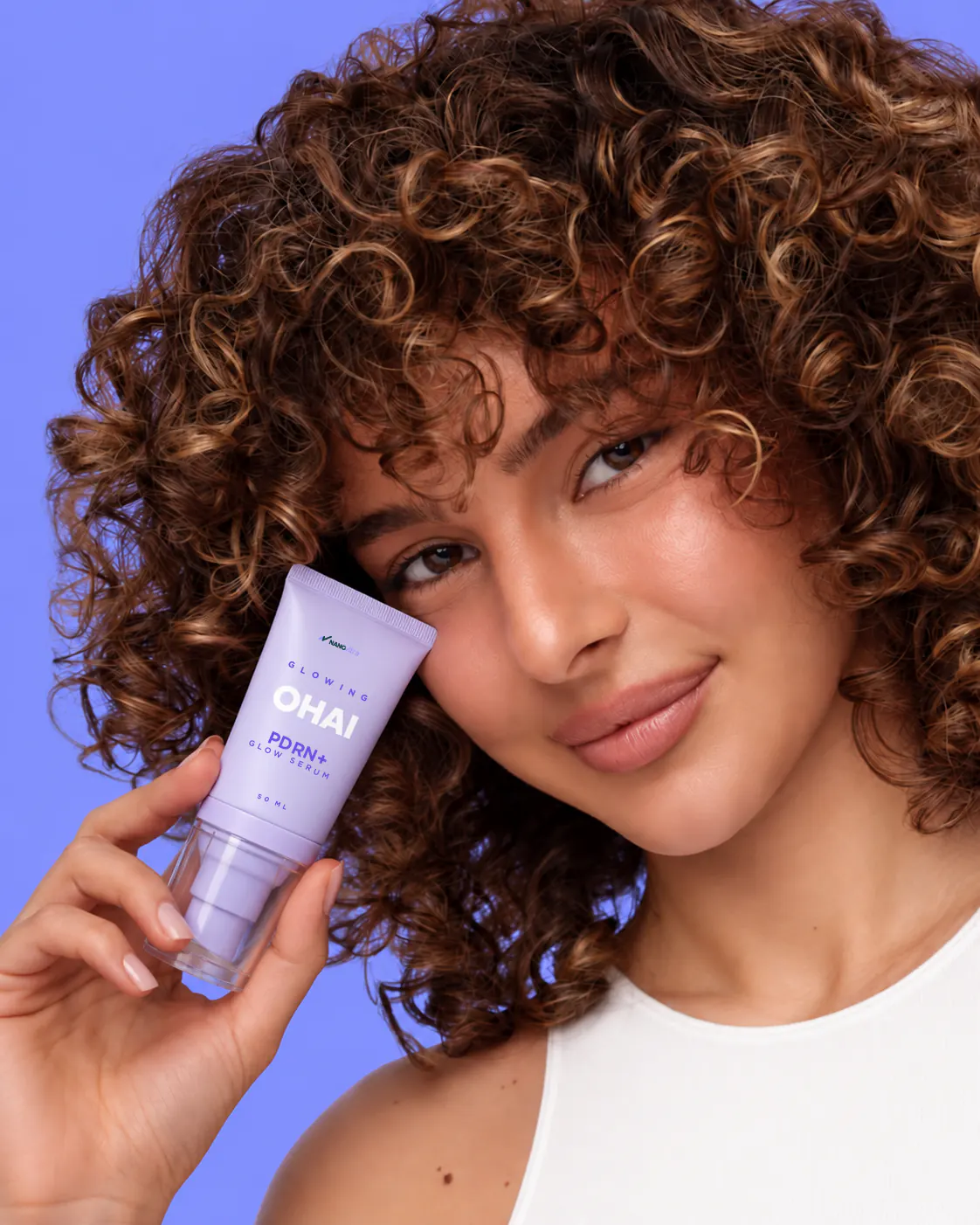 Model with curly hair holding a lavender tube of OHAI PDRN+ Glow Serum